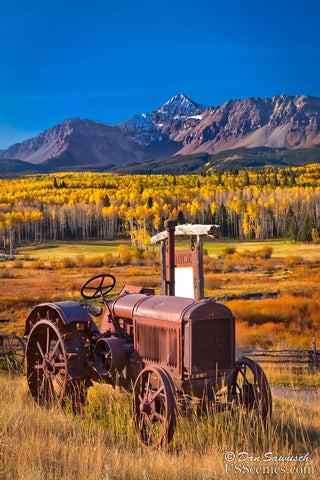 an old tractor sits in front of wilson peak and yellow fall aspens near telluride colorado